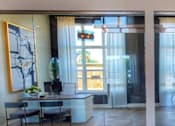 Thumbnail 14 of 17 - A modern room with a glass table and chairs, a TV, and a large abstract painting on the wall.