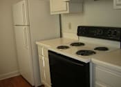 Thumbnail 2 of 6 - A black stove top oven with four burners and a white refrigerator in a kitchen.