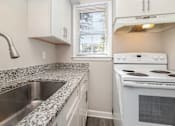 Thumbnail 6 of 23 - A white stove is in a kitchen with granite countertops.