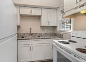 Thumbnail 10 of 23 - A white kitchen with a stove, sink, and cabinets.
