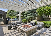 Thumbnail 17 of 40 - A patio with a fire pit and seating area under a white pergola.