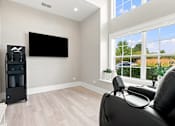 Thumbnail 21 of 39 - A black leather chair is in front of a flat screen TV in a room with a large window.