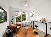 Thumbnail 20 of 46 - A room with a brown leather couch, a black stool, a white desk, and a brown rug.