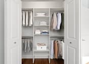 Thumbnail 16 of 32 - A white closet with clothes hanging and shelves with items.