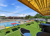Thumbnail 8 of 20 - A yellow umbrella shades a table and chairs on a lawn next to a pool.