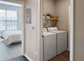 Thumbnail 40 of 47 - A small bedroom with a bed, laundry basket, and washing machine.