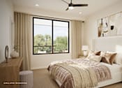 Thumbnail 3 of 7 - Rendering of bright townhome apartment bedroom with upholstered bed, neutral finishes, ceiling fan, and large window with balcony and tree views.
