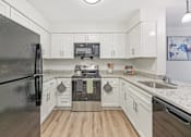 Thumbnail 15 of 36 - A kitchen with a black refrigerator and white cabinets.