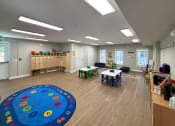 Thumbnail 11 of 32 - a preschool classroom with tables and chairs and a blue rug in the center