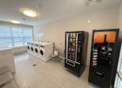 Thumbnail 16 of 75 - A room with a washing machine, a vending machine, and a fridge.