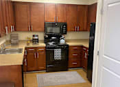 Thumbnail 2 of 9 - A kitchen with wooden cabinets and a black stove top oven.