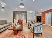 Thumbnail 26 of 32 - A living room with a grey sofa, a wooden coffee table, and a patterned armchair.