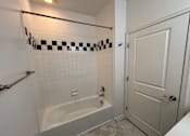 Thumbnail 19 of 30 - A white bathroom with a checkered tile border on the shower.