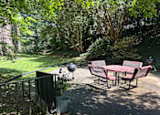 Thumbnail 7 of 8 - A patio with a table and chairs and a grill.