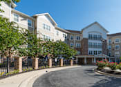 Thumbnail 3 of 17 - A large apartment complex with a driveway in front.
