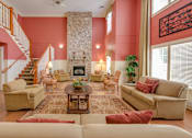 Thumbnail 6 of 17 - A living room with a stone fireplace and a staircase.