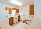 Thumbnail 15 of 17 - A kitchen with a white refrigerator, wooden cabinets, and a white stove top oven.