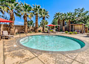 Thumbnail 22 of 41 - A pool surrounded by palm trees and a patio area with chairs and umbrellas.