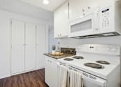Thumbnail 17 of 24 - A white kitchen with a stove, microwave, and cabinets.