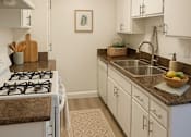Thumbnail 8 of 23 - A galley kitchen with white cabinets and a brown rug.