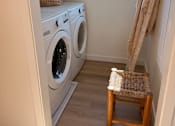 Thumbnail 7 of 27 - A small laundry room with a chair and a basket on top of the washing machine.