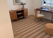 Thumbnail 12 of 27 - A room with a desk, chair, and a cabinet with a vase on top.