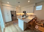 Thumbnail 1 of 27 - A kitchen with a white counter and wooden chairs.