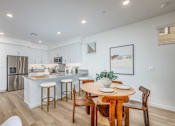 Thumbnail 25 of 27 - A kitchen with a table and chairs in the foreground and a fridge and microwave in the background.