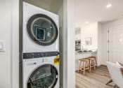 Thumbnail 24 of 27 - A modern laundry room with a washing machine and a view into a kitchen.