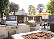 Thumbnail 21 of 34 - A patio with a grill and chairs under yellow umbrellas.