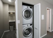Thumbnail 8 of 34 - A white washing machine is in a small laundry room.