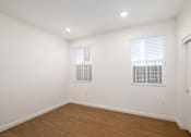 Thumbnail 19 of 33 - A room with wooden floors and two windows with blinds.