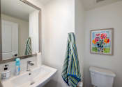 Thumbnail 15 of 33 - A bathroom with a white toilet, a white sink, a mirror, and a picture of flowers on the wall.