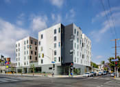 Thumbnail 1 of 29 - A modern building with a white and grey exterior is situated on a street corner with cars and traffic lights.