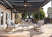 Thumbnail 12 of 34 - A patio with a white couch, two chairs, and a table under a pergola.