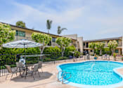 Thumbnail 1 of 13 - A swimming pool surrounded by chairs and umbrellas in front of a building.