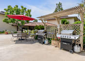 Thumbnail 7 of 13 - A patio with a grill and a table under a red umbrella.