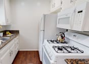 Thumbnail 16 of 25 - A white kitchen with a stove, sink, and cabinets.