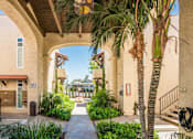 Thumbnail 13 of 25 - A pathway leads through a courtyard with a palm tree and a building with a red tile roof.