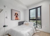 Thumbnail 6 of 29 - A bedroom with a bed, a lamp, and a picture of a dog on the wall.
