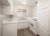 Thumbnail 4 of 32 - A white kitchen with a stove, sink, and cabinets.