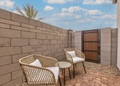 Thumbnail 4 of 31 - a patio with two chairs and a table next to a brick wall at Village of Chandler Apartments, Chandler, AZ, 85249