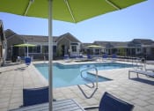 Thumbnail 13 of 31 - a swimming pool with chairs and umbrellas in front of a house at Village of Chandler Apartments, Chandler, Arizona