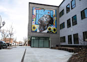 Thumbnail 10 of 19 - A mural of a man with flowers is on the side of a building.