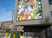 Thumbnail 11 of 19 - A large mural on a building's side depicts a group of people.