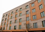 Thumbnail 8 of 10 - A tall building with orange and beige panels and windows.