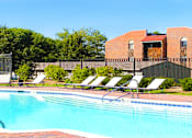 Thumbnail 2 of 20 - Swimming pool with sundeck, pool-side lounge chairs, and park-like setting at Inwood Apartments in La Vista, Nebraska
