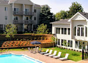 Thumbnail 2 of 27 - Swimming pool with sundeck and poolside lounge chairs, beautiful landscaping, lush landscaping, apartments with pool view, and park-like setting at Kensington Woods Apartments in Omaha, Nebraska
