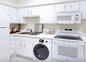 Thumbnail 17 of 42 - A white kitchen with a washing machine and a microwave.
