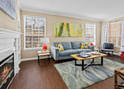 Thumbnail 15 of 25 - Spacious living room with wood-burning fireplace with glass doors, hardwood floors, and oversized windows Tuscany Park Apartments in Houston.
